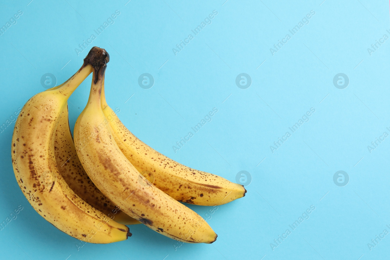 Photo of Bunch of ripe bananas with dark spots on light blue background, top view. Space for text