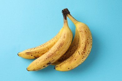 Bunch of ripe bananas with dark spots on light blue background, top view