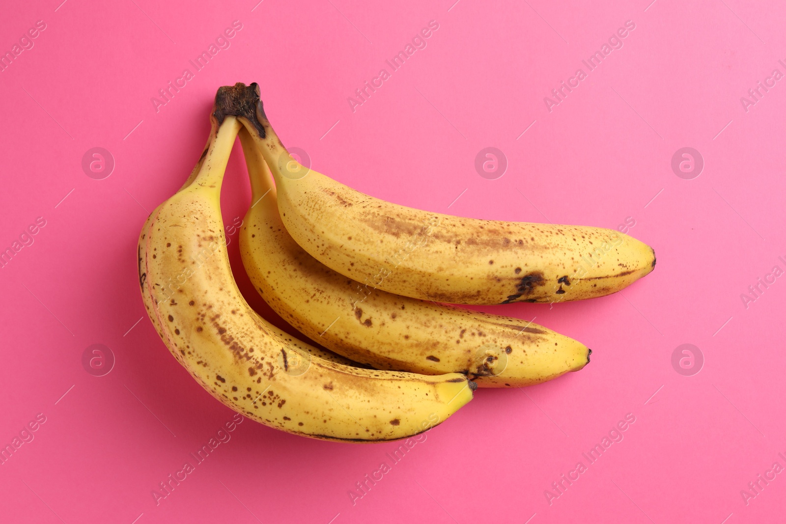 Photo of Bunch of ripe bananas with dark spots on pink background, top view