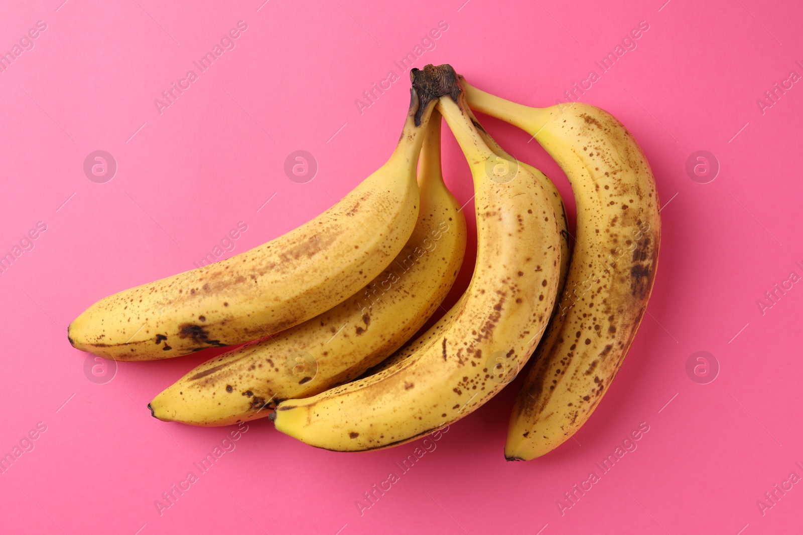 Photo of Bunch of ripe bananas with dark spots on pink background, top view