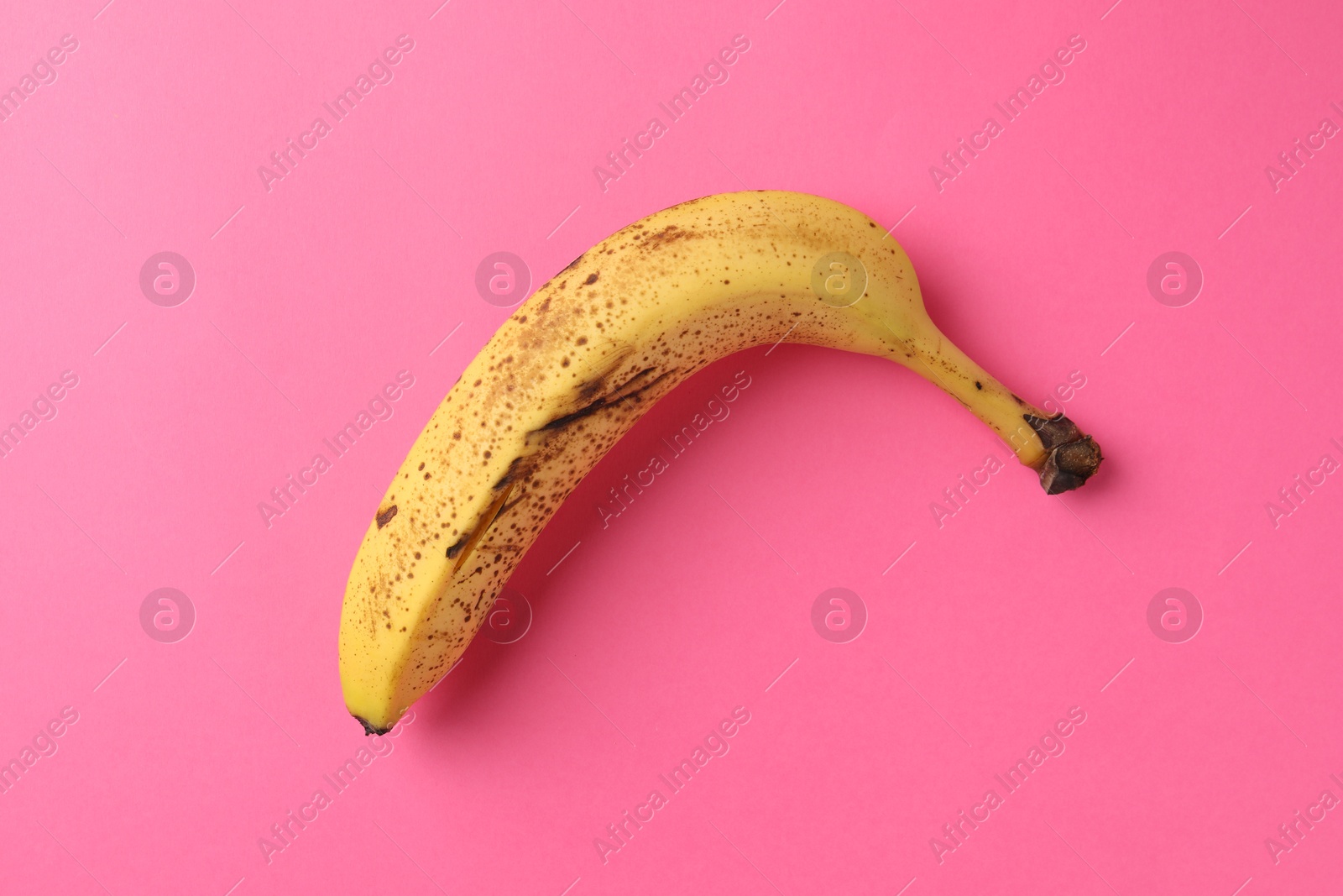 Photo of Ripe banana with dark spots on pink background, top view