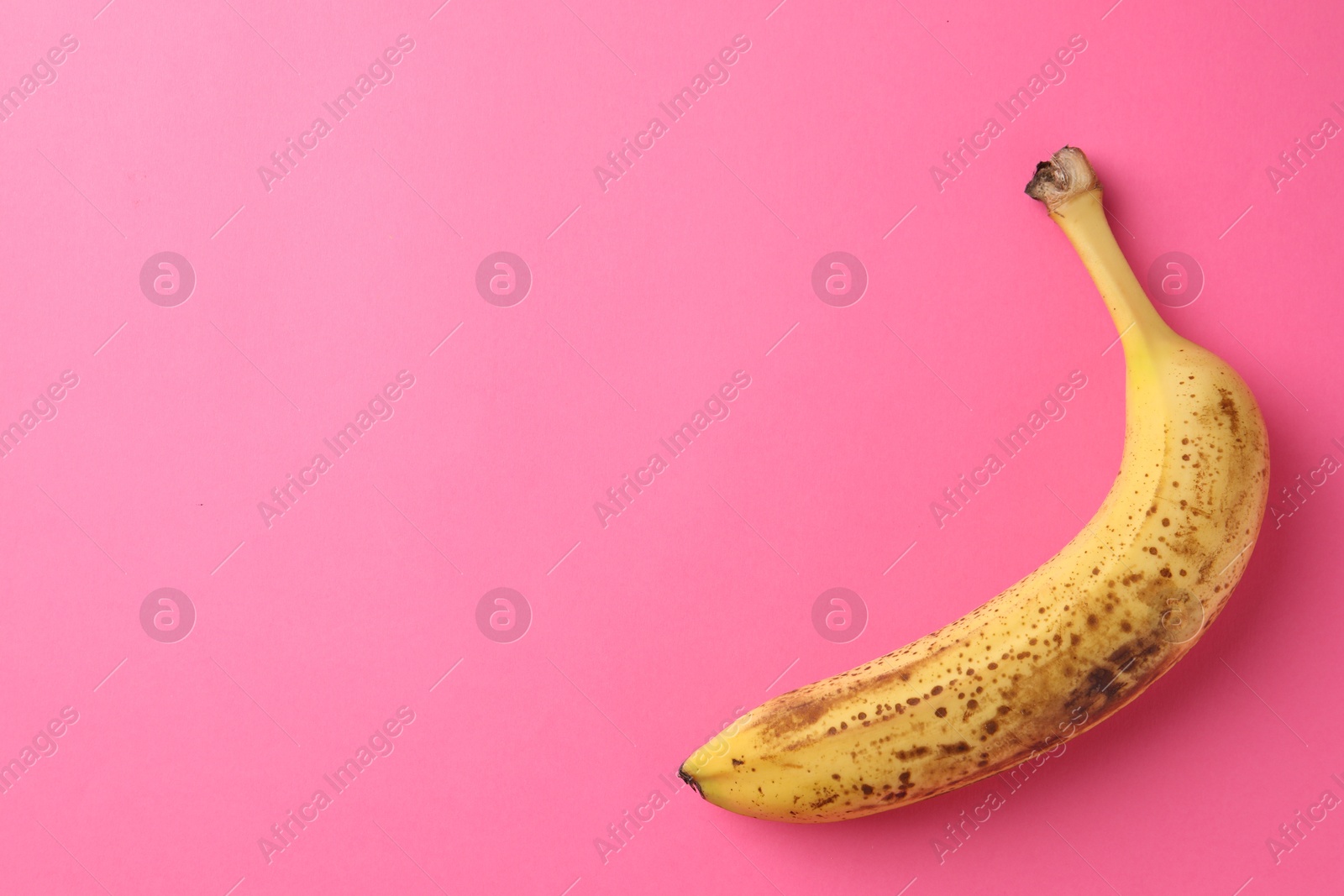 Photo of Ripe banana with dark spots on pink background, top view. Space for text