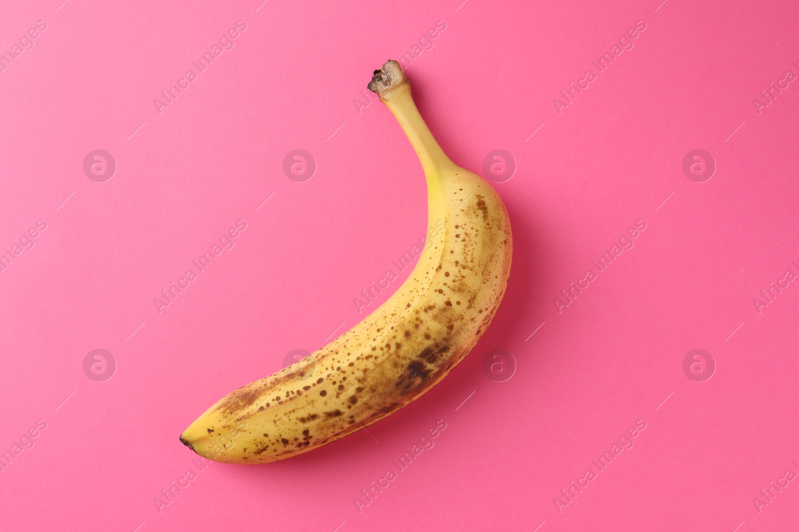 Photo of Ripe banana with dark spots on pink background, top view