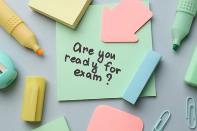 Paper note with question Are You Ready For Exam and stationery on grey background, flat lay