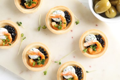 Delicious canapes with shrimps and olives on white table, top view