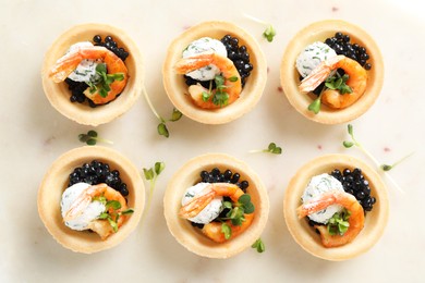 Delicious canapes with shrimps and black caviar on light table, top view