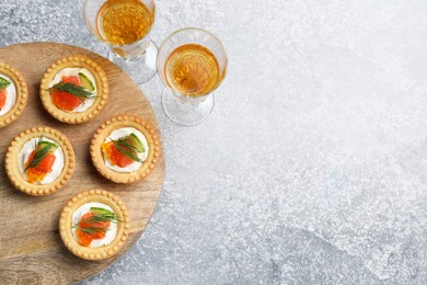 Delicious canapes with salmon and glasses of white wine on gray table, flat lay. Space for text