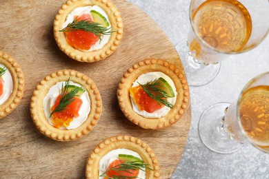 Delicious canapes with salmon and glasses of white wine on gray table, flat lay