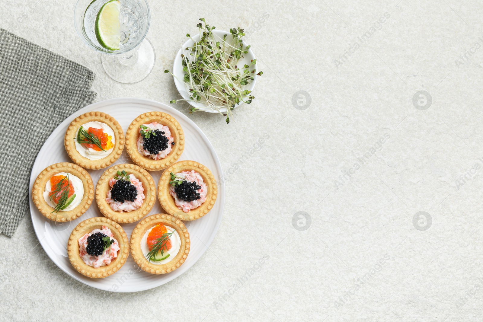 Photo of Delicious canapes with salmon, caviar, microgreens and glass of water on beige textured table, flat lay. Space for text