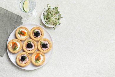 Delicious canapes with salmon, caviar, microgreens and glass of water on beige textured table, flat lay. Space for text