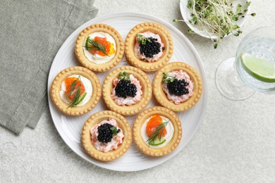 Delicious canapes with salmon, caviar, microgreens and glass of water on beige textured table, flat lay