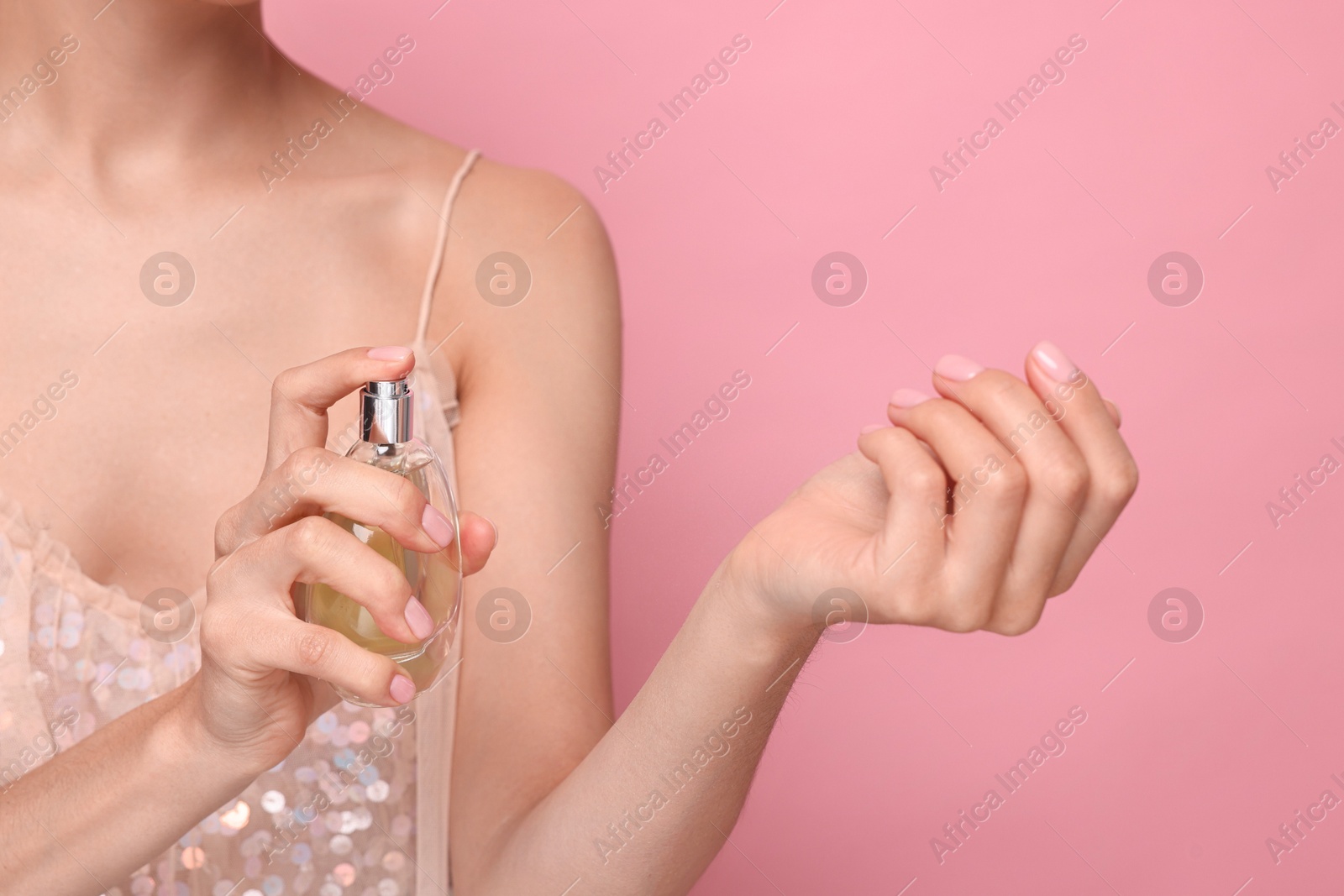 Photo of Woman spraying perfume onto wrist against pink background, closeup