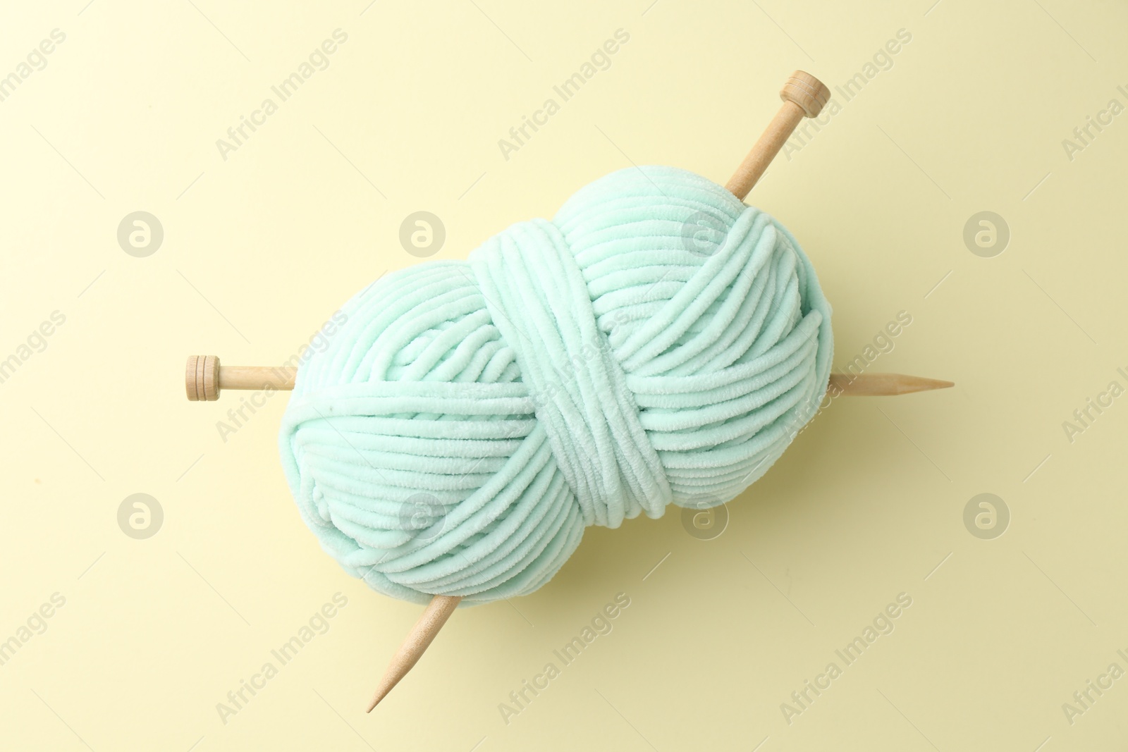 Photo of Skein of plush yarn with knitting needles on beige background, top view