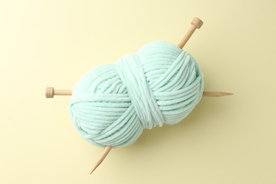 Photo of Skein of plush yarn with knitting needles on beige background, top view