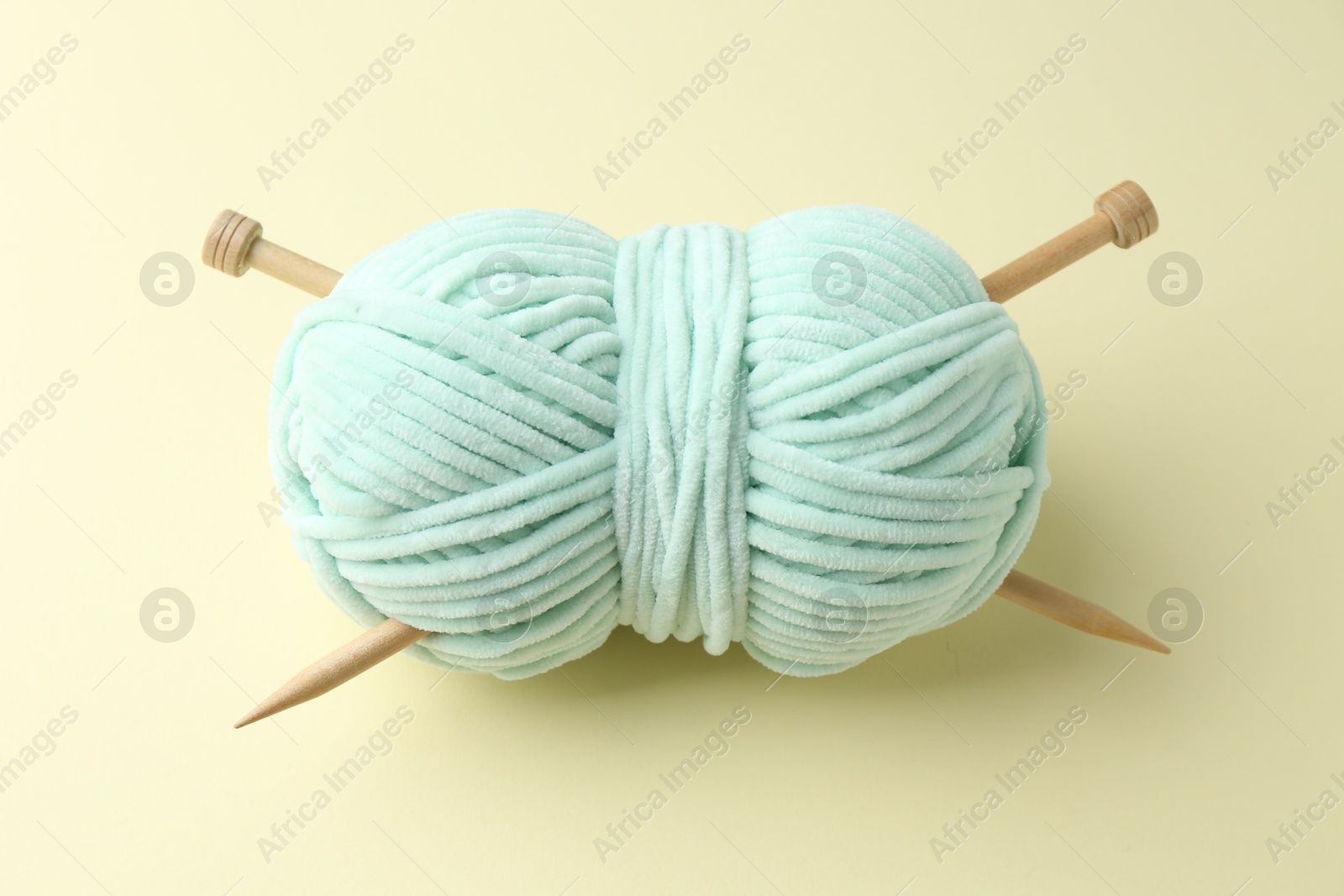 Photo of Skein of plush yarn with knitting needles on beige background, above view