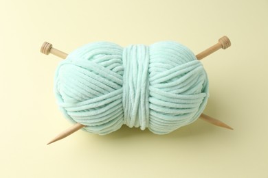 Photo of Skein of plush yarn with knitting needles on beige background, above view