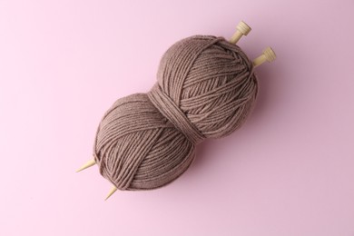 Photo of Skein of brown yarn with knitting needles on pink background, top view