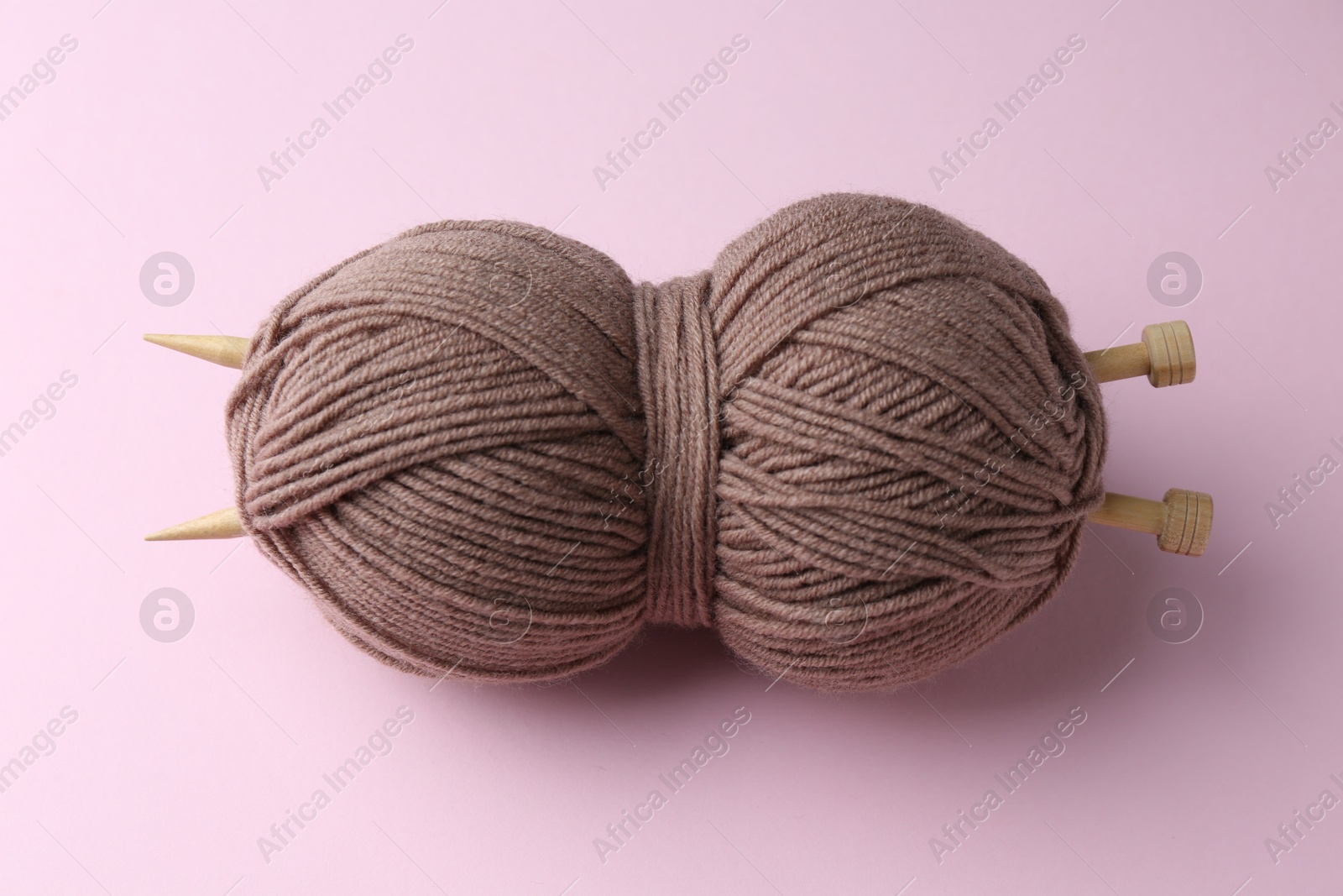 Photo of Skein of brown yarn with knitting needles on pink background, above view