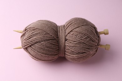 Skein of brown yarn with knitting needles on pink background, above view