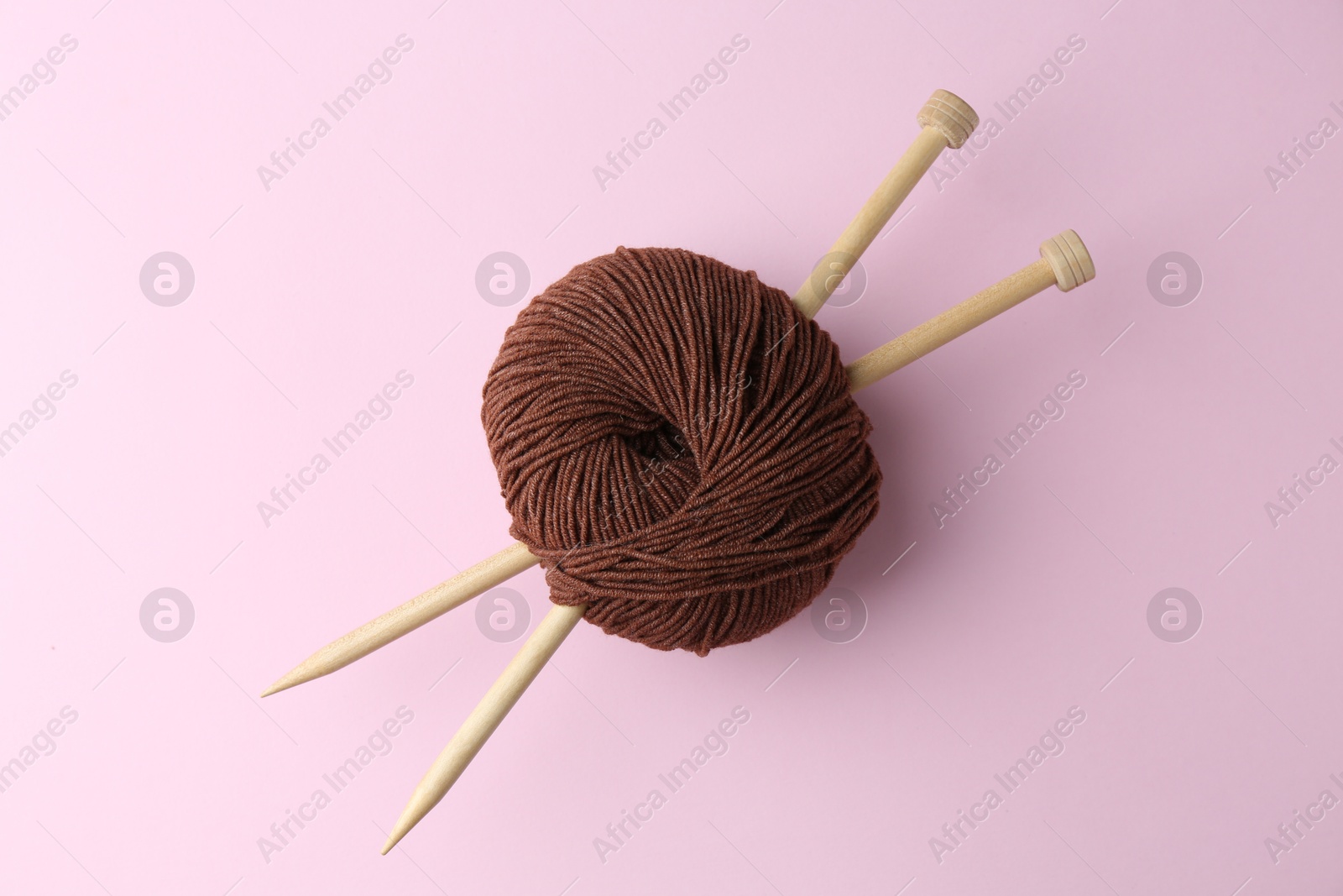 Photo of Brown yarn with knitting needles on pink background, top view