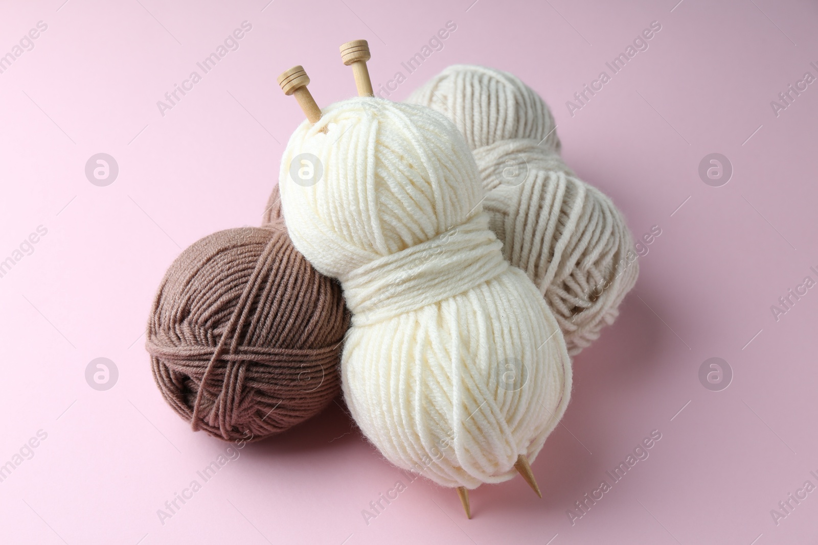 Photo of Skeins of yarn and knitting needles on pink background