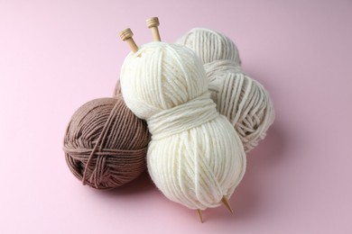 Skeins of yarn and knitting needles on pink background