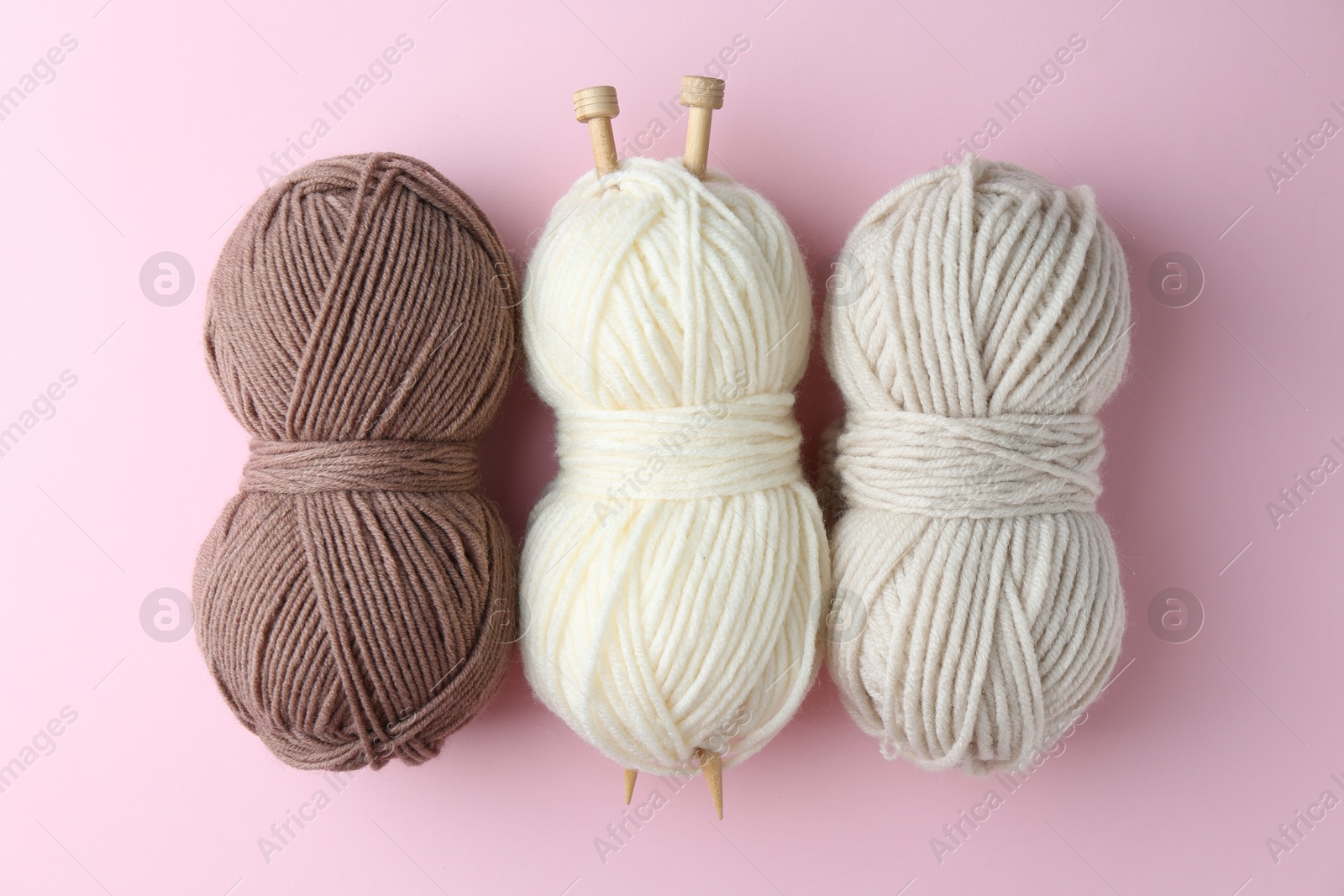 Photo of Different skeins of yarn and knitting needles on pink background, flat lay