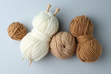 Skeins of yarn and knitting needles on light grey background, flat lay