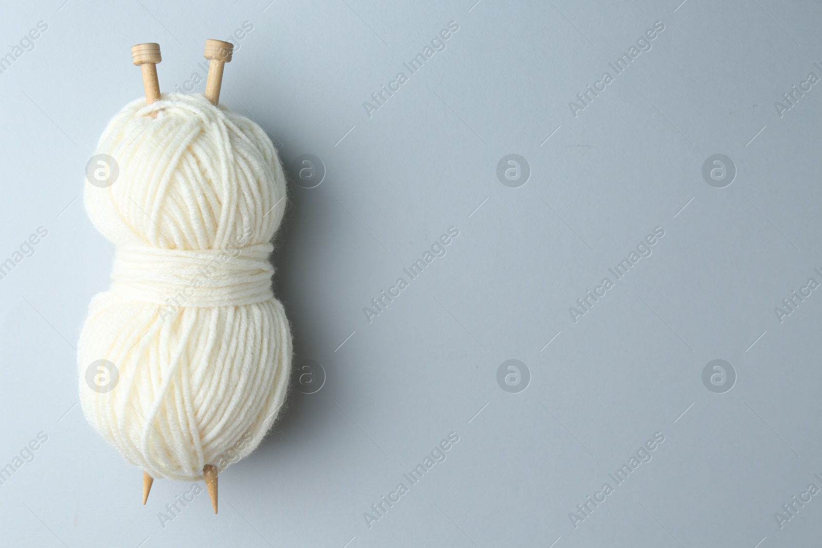 Photo of White yarn with knitting needles on light grey background, top view. Space for text