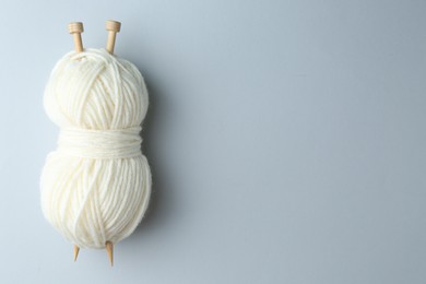 Photo of White yarn with knitting needles on light grey background, top view. Space for text