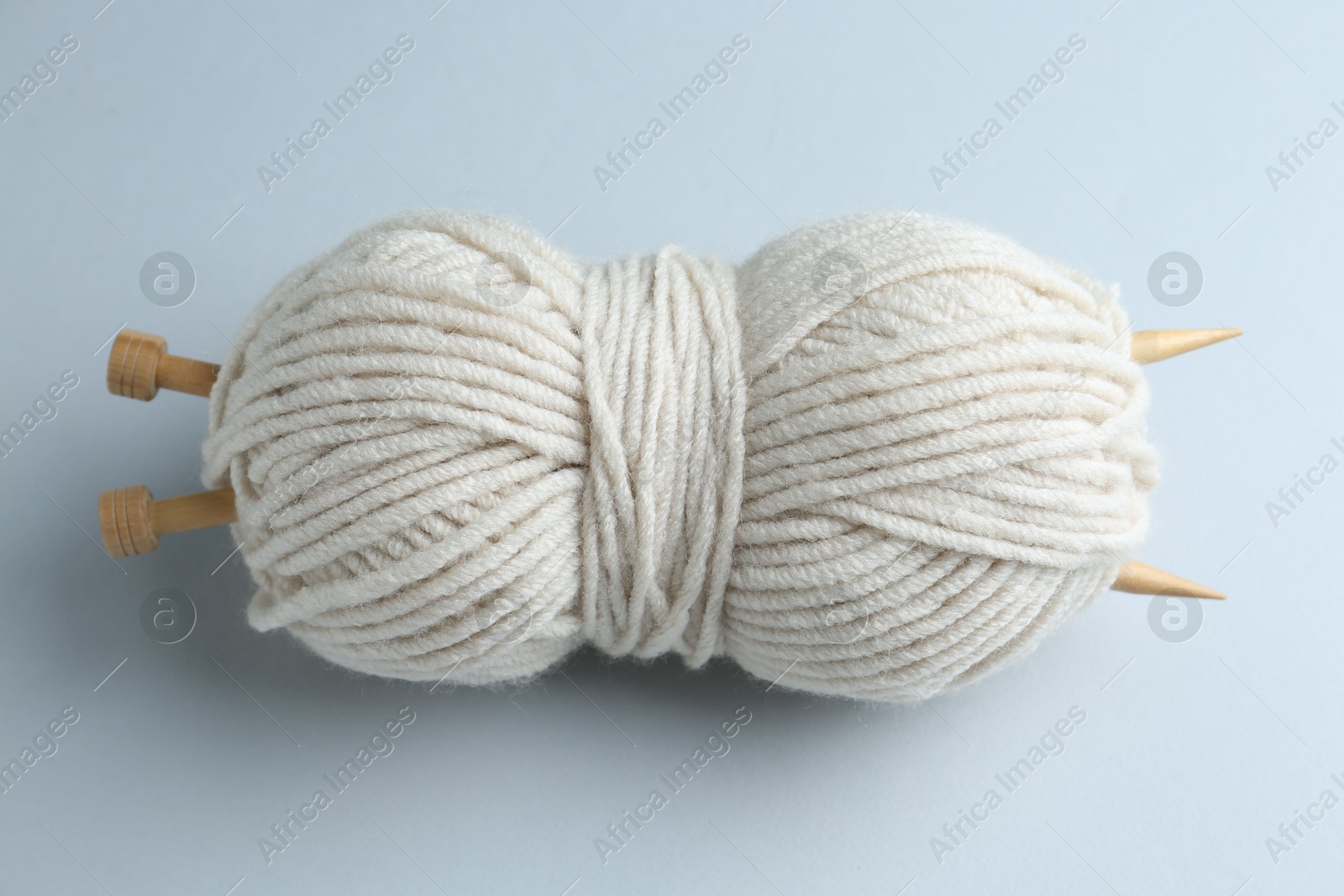 Photo of White yarn with knitting needles on light grey background, above view