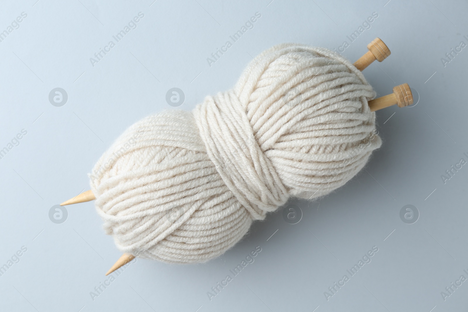 Photo of White yarn with knitting needles on light grey background, top view