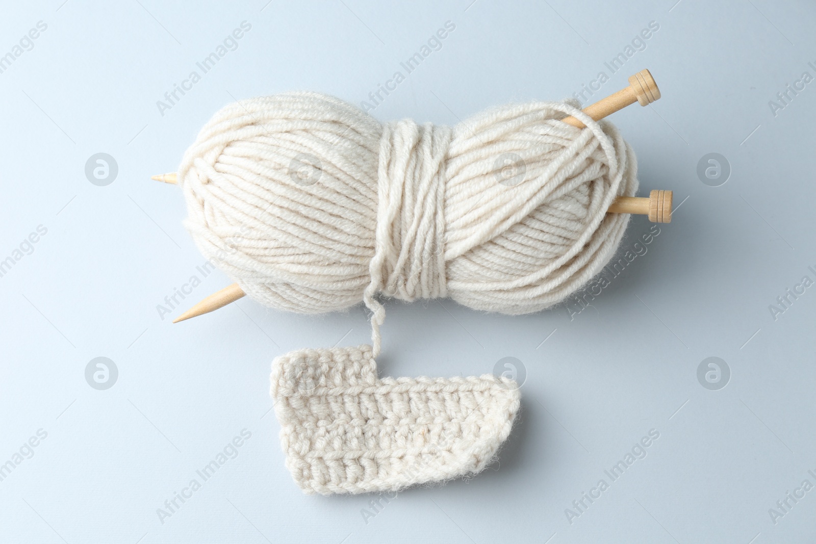 Photo of White yarn with knitting needles and pattern sample on light grey background, top view