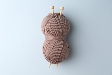 Brown yarn with knitting needles on light grey background, top view