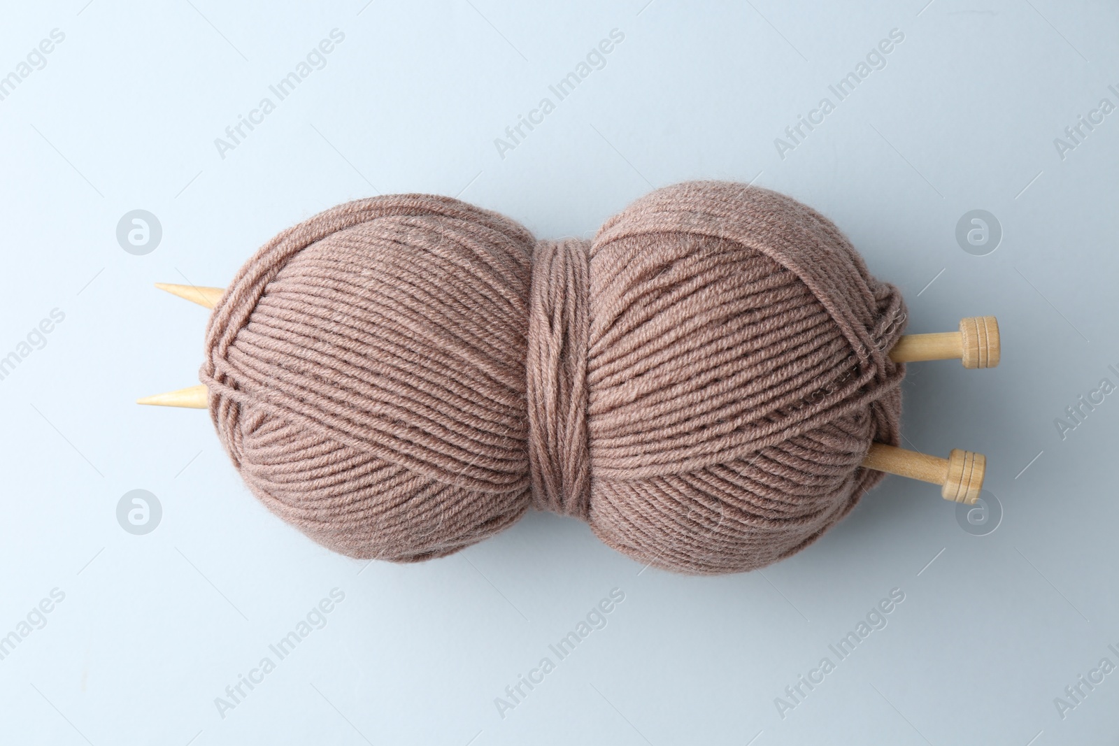 Photo of Brown yarn with knitting needles on light grey background, top view