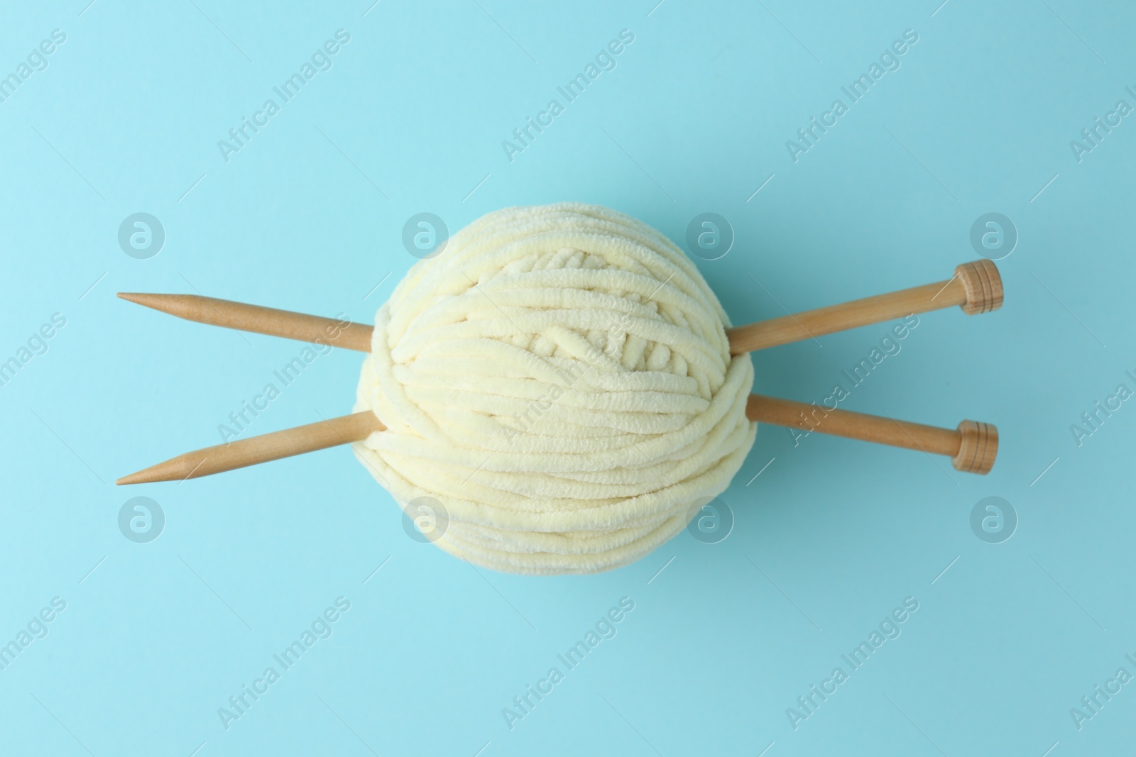 Photo of Ball of plush yarn with knitting needles on light blue background, top view