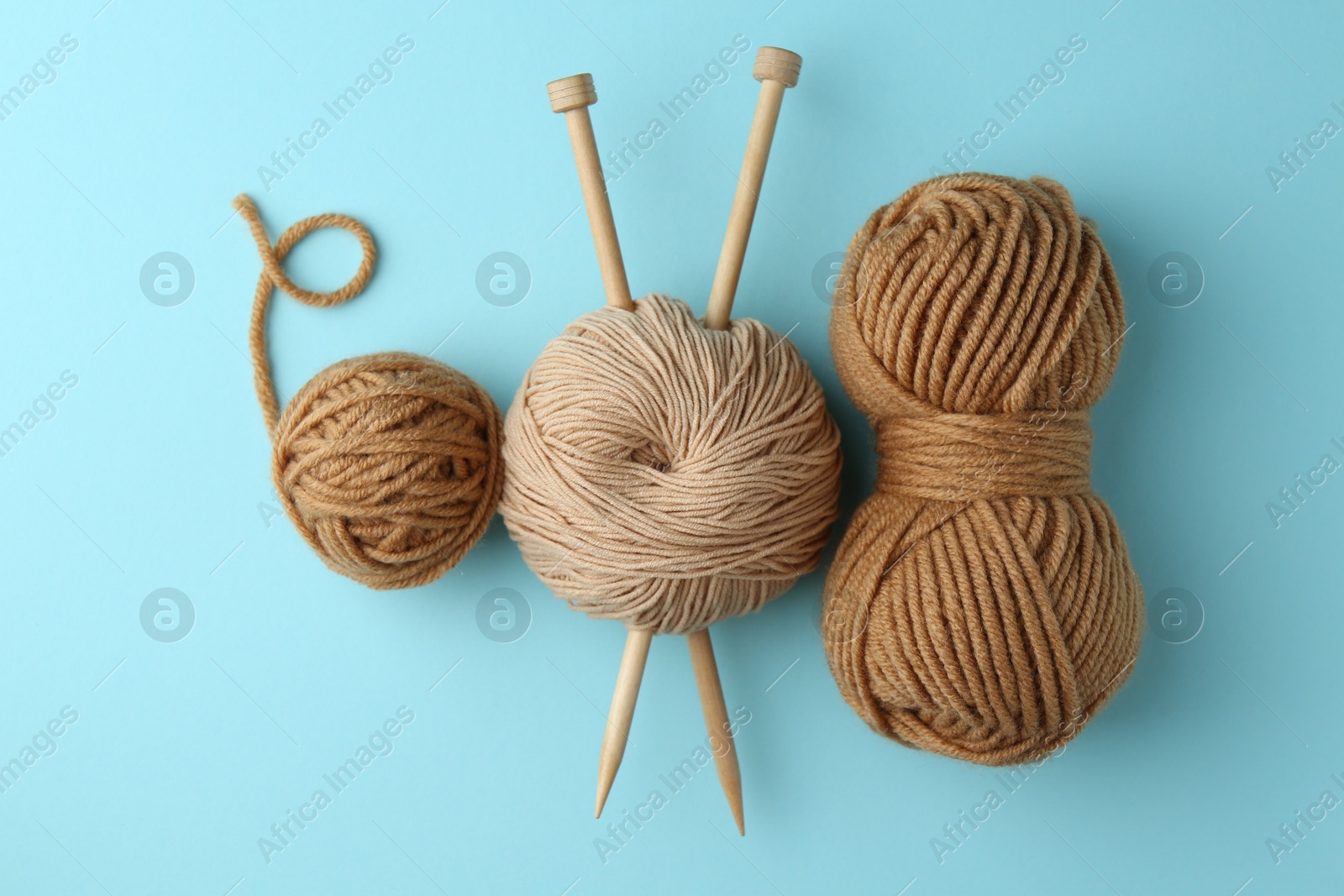 Photo of Skeins of yarn and knitting needles on light blue background, flat lay