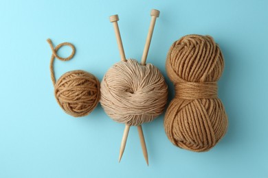 Skeins of yarn and knitting needles on light blue background, flat lay