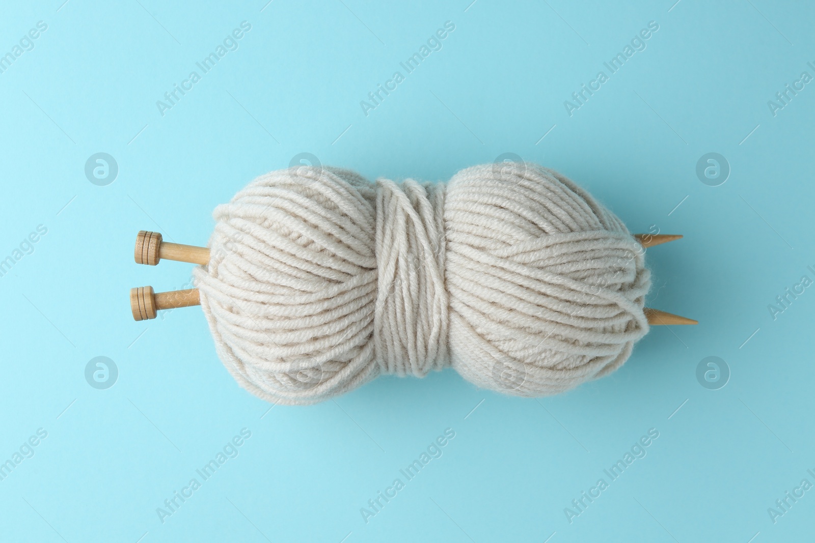 Photo of White yarn with knitting needles on light blue background, top view