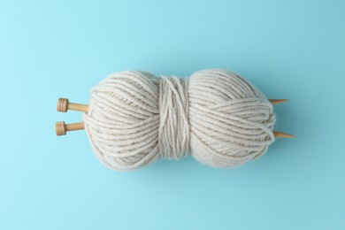 White yarn with knitting needles on light blue background, top view