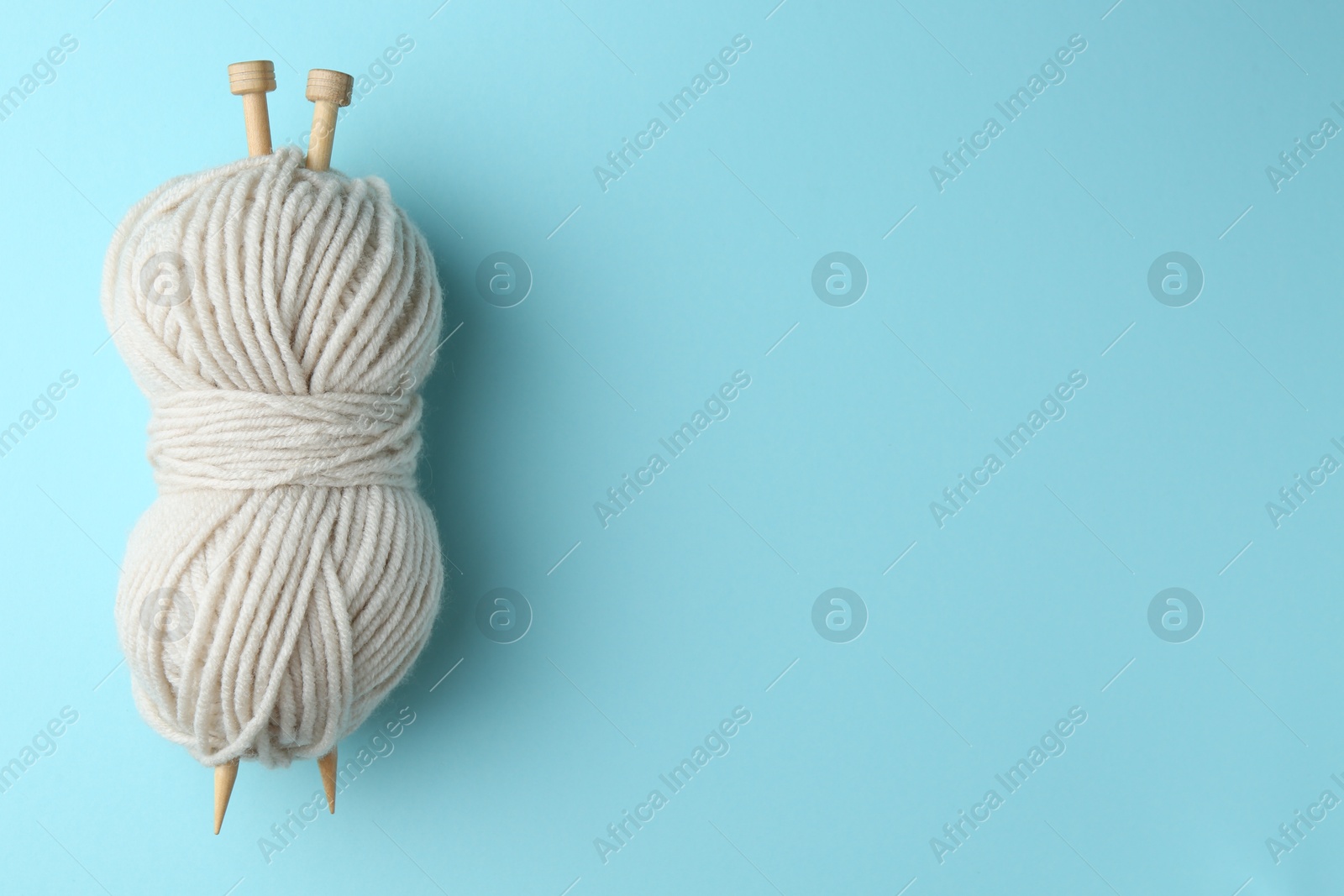 Photo of White yarn with knitting needles on light blue background, top view. Space for text