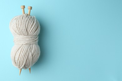 Photo of White yarn with knitting needles on light blue background, top view. Space for text