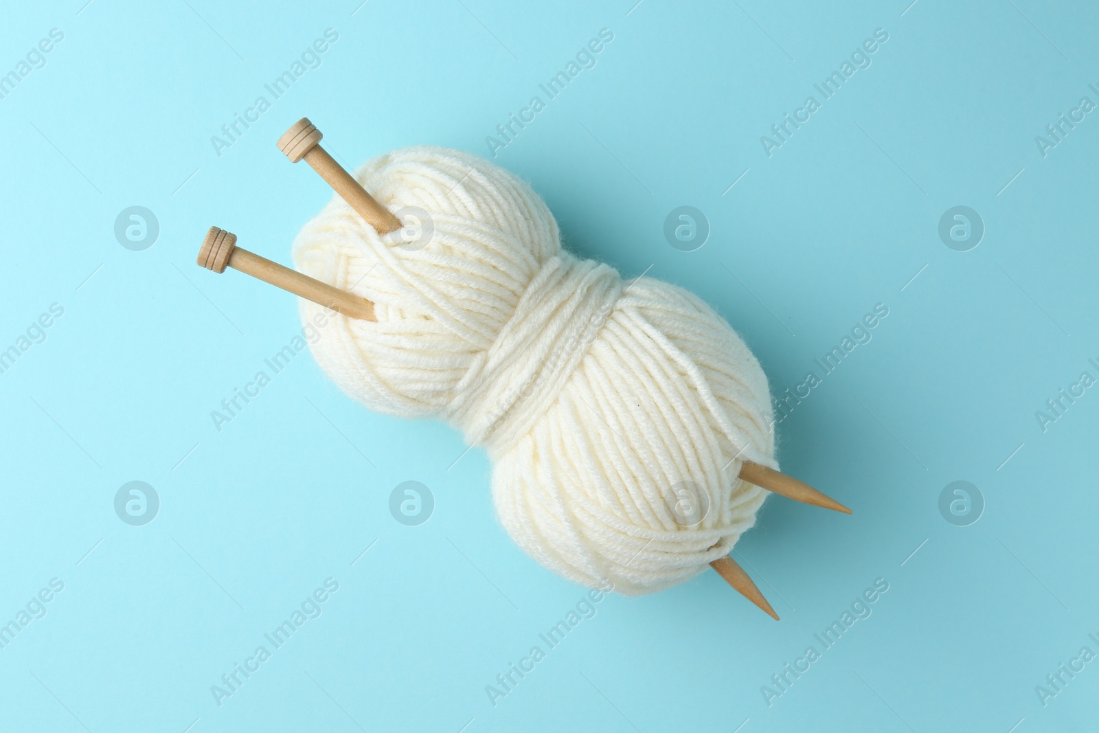 Photo of White yarn with knitting needles on light blue background, top view