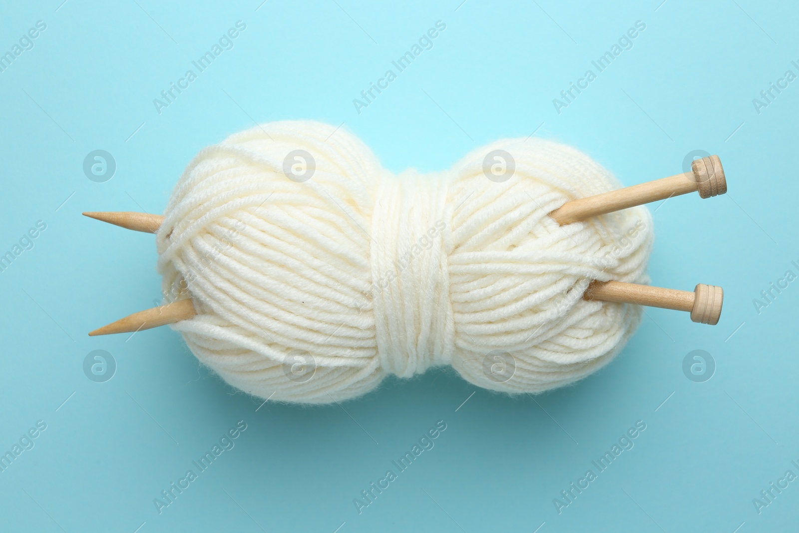 Photo of White yarn with knitting needles on light blue background, above view