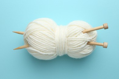 White yarn with knitting needles on light blue background, above view