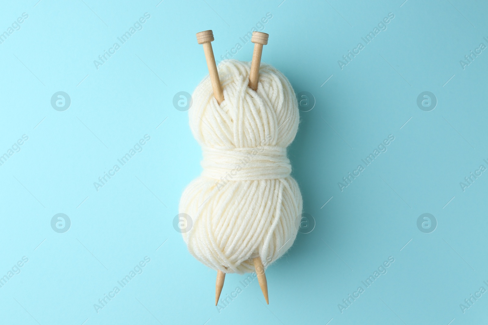 Photo of White yarn with knitting needles on light blue background, top view