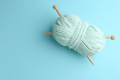 Plush yarn with knitting needles on light blue background, top view. Space for text