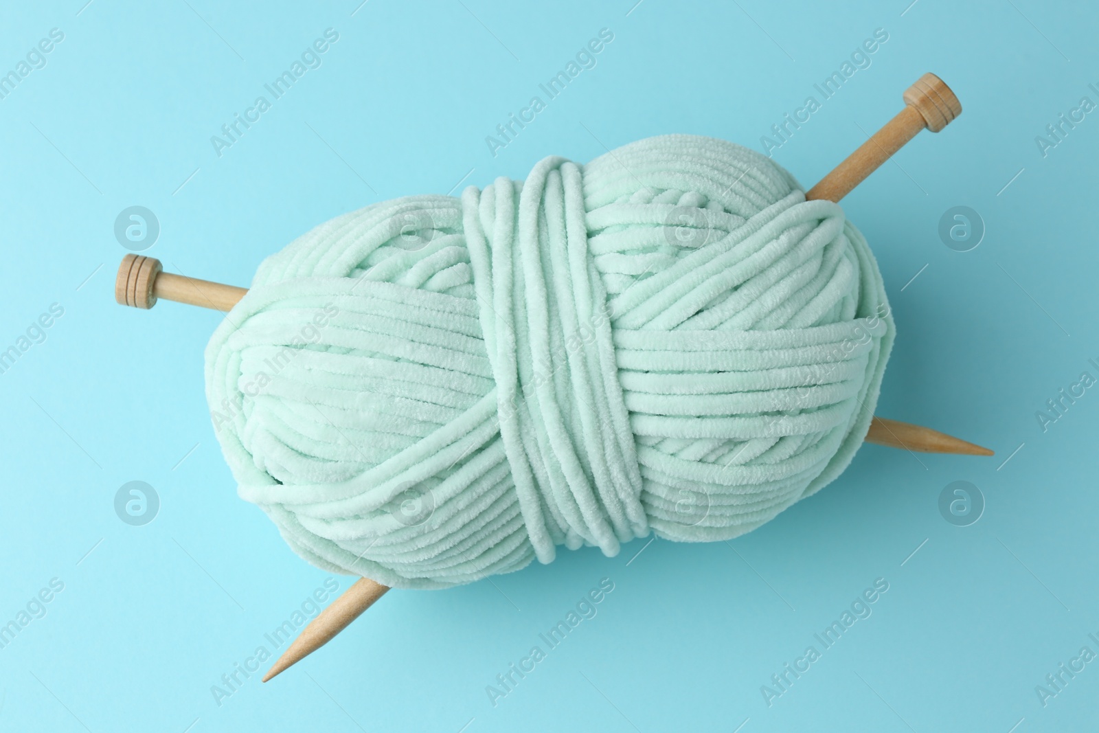 Photo of Plush yarn with knitting needles on light blue background, top view