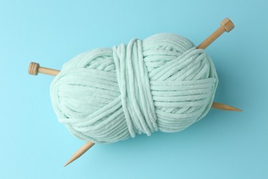 Photo of Plush yarn with knitting needles on light blue background, top view