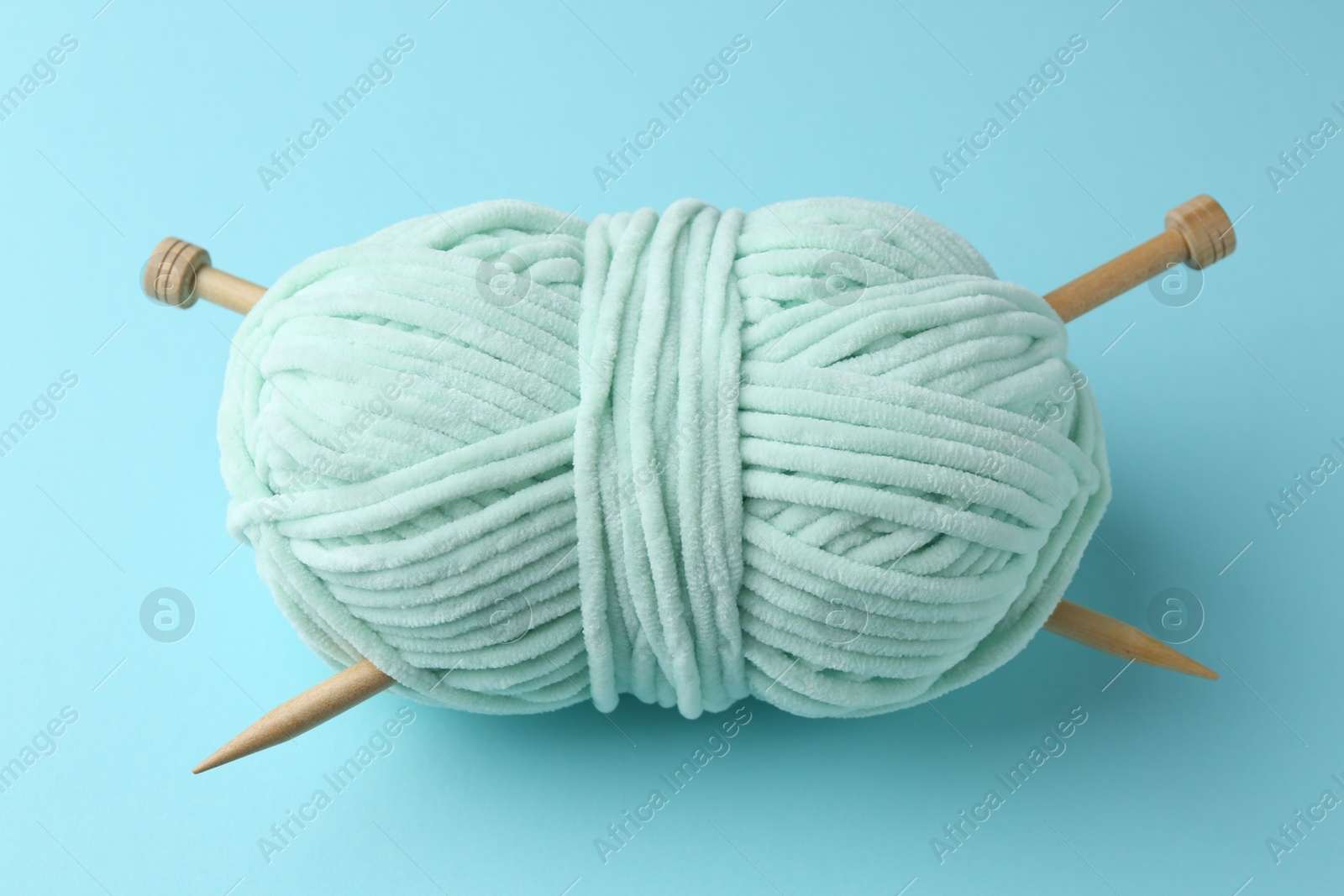 Photo of Plush yarn with knitting needles on light blue background